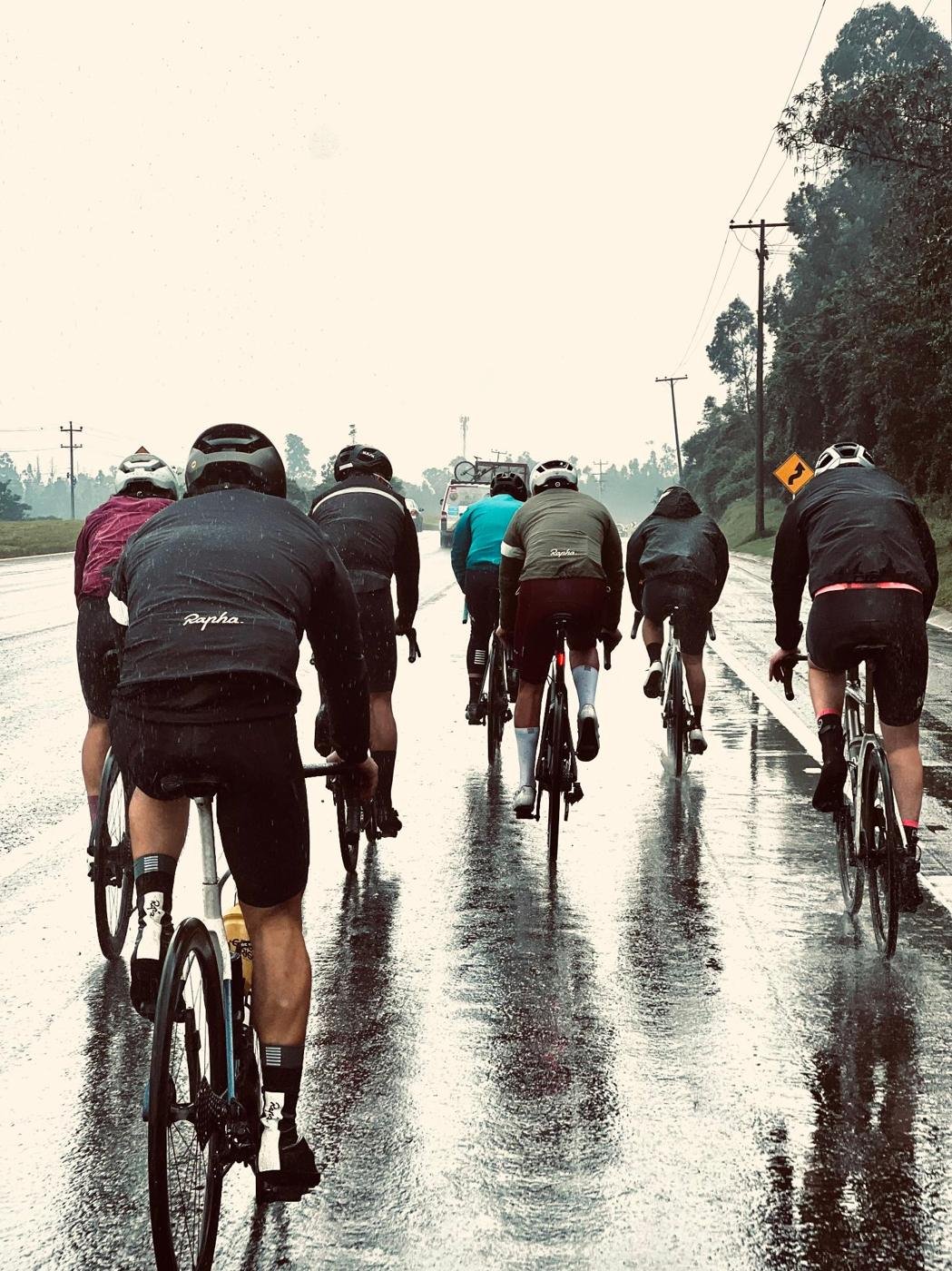 Grupo de ciclistas rodando bajo la lluvia por una carretera de la sabana